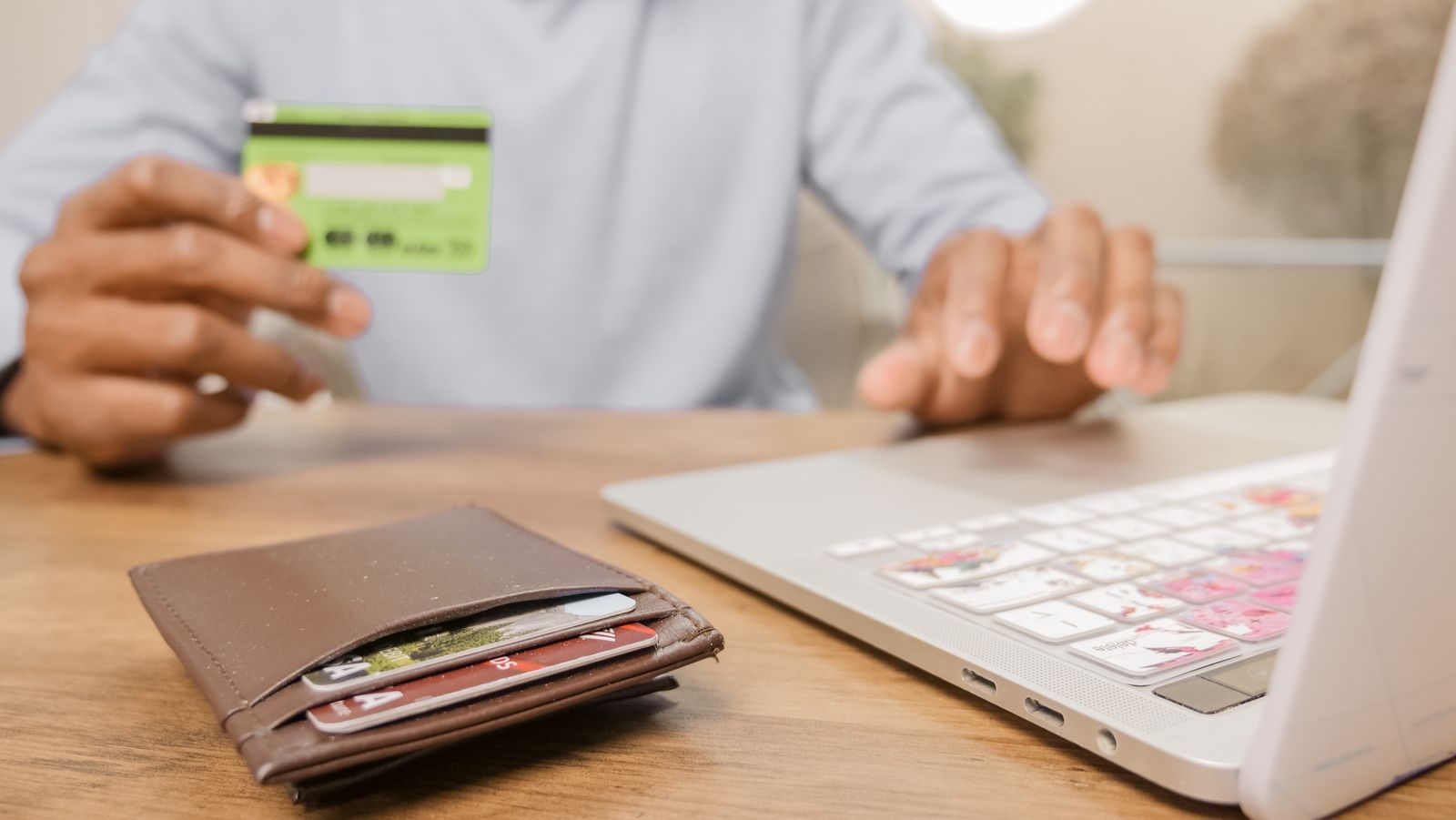 A person holding a green card over a wallet while typing on a laptop to book a cruise with card points