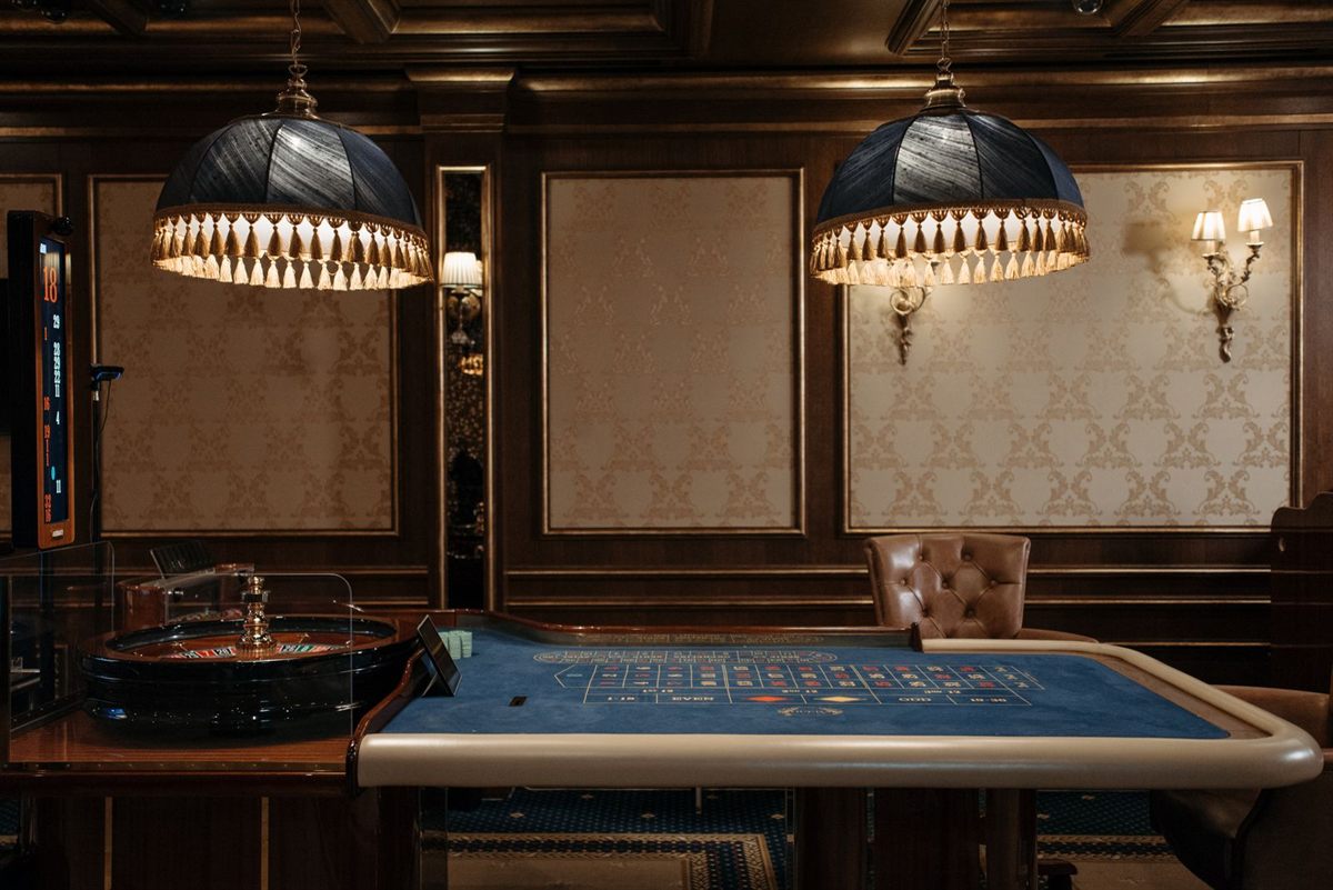 A quiet, wood-panelled gaming room with a roulette table under two pendant lamps