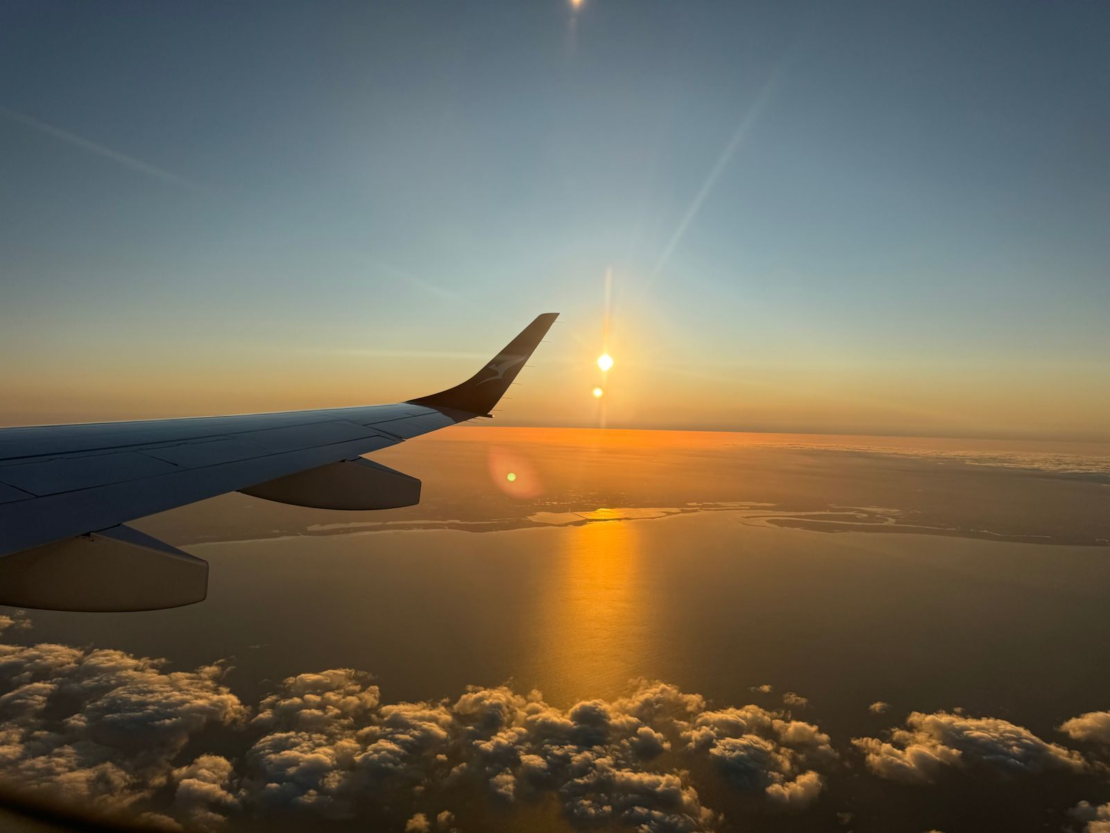 An airplane wing over a sea of clouds as the sun sets on the horizon