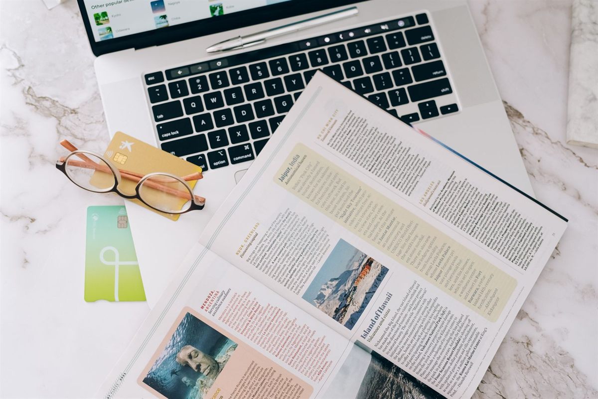 Payment cards, reading glasses and a travel magazine on an open laptop