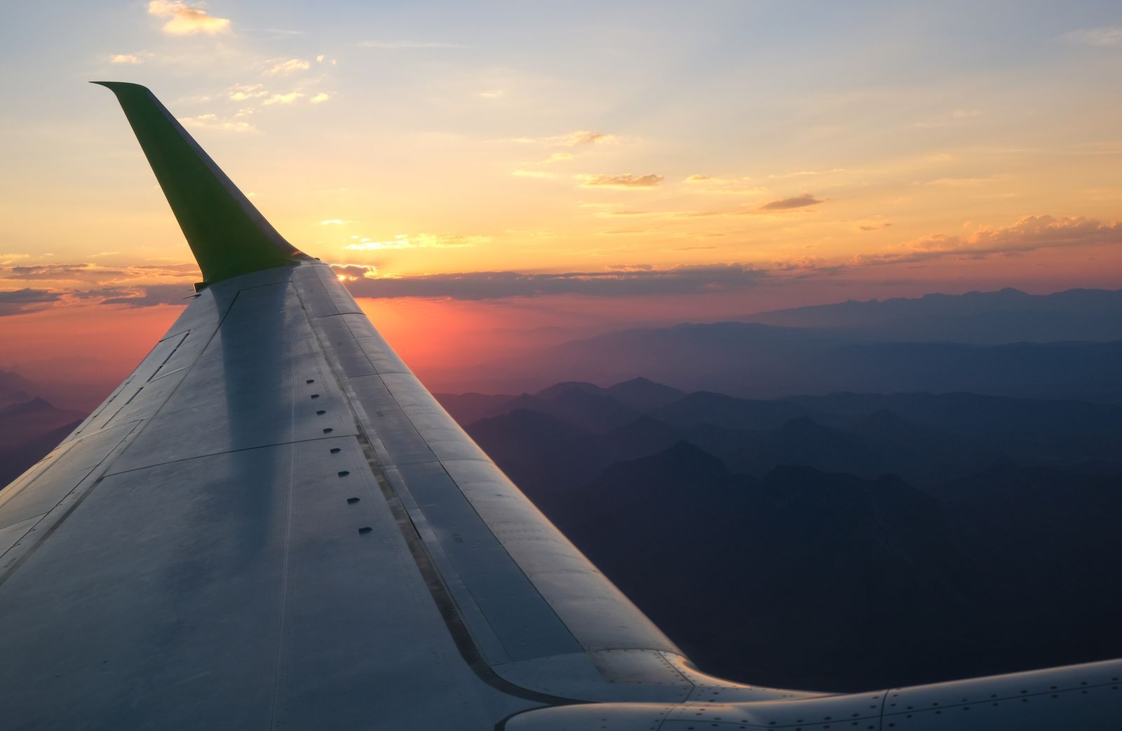 Looking along an airplane wing at sunset above the clouds, the flight to a cruise paid with airline miles